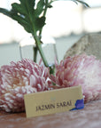 A table with two artificial pink roses and a card with the name 'Jazmin Saraé' on it, placed on a table with a blurred background.