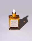 A clear glass bottle with a dropper filled with yellow liquid, labeled 'JASMINUM', on a shadowed background.