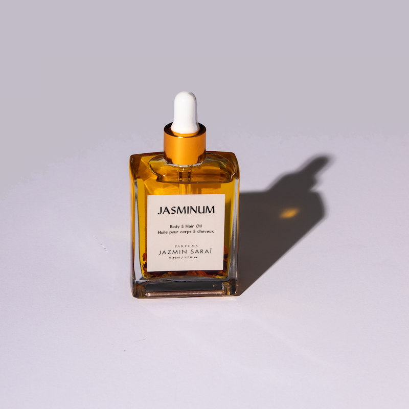 A clear glass bottle with a dropper filled with yellow liquid, labeled 'JASMINUM', on a shadowed background.